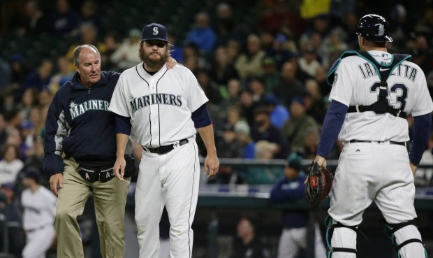 Seattle Mariners starting pitcher Wade Miley, second from left, stands with trainer Rick Griffin, after Miley collided with catcher Chris Iannetta, right, as they tried to field a bunt single by Texas Rangers' Delino DeShields during the third inning of a baseball game, Tuesday, April 12, 2016, in Seattle. (AP Photo/Ted S. Warren)