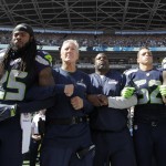 Seattle Seahawks players and coaches, including cornerback Richard Sherman (25) and head coach Pete Carroll, third from left, stand and link arms during the singing of the national anthem before an NFL football game against the Miami Dolphins, Sunday, Sept. 11, 2016, in Seattle. (AP Photo/Elaine Thompson)