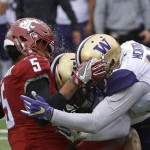 Rain water comes off the helmet of Washington State wide receiver Isaiah Johnson-Mack, left, as he is hit by Washington defensive back Jojo McIntosh, right, and linebacker DJ Beavers, center, on an incomplete pass play in the first half of an NCAA college football game, Friday, Nov. 25, 2016, in Pullman, Wash. (AP Photo/Ted S. Warren)