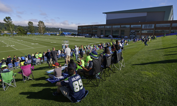 Early arriving fans sit on a grass hill overlooking the Seattle Seahawks NFL football training camp...