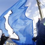 Former Seattle Seahawks player Lawyer Milloy, right, works against 40 mph winds to raise a "12 Flag," a show of support of Seahawks' fans, atop the Space Needle Friday, Jan. 4, 2019, in Seattle. The flag will fly in celebration of the team's wild card playoff game in Dallas on Saturday against the Cowboys and will remain up through Sunday, Jan. 6. (AP Photo/Elaine Thompson)