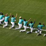 SEATTLE, WASHINGTON - JULY 31: (L-R) Shed Long Jr. #4, Kyle Lewis #1, Joe Thurston #27, Justin Dunn #35, Carl Edwards Jr., Dee Gordon #9, Mallex Smith #0 and J.P. Crawford #3 of the Seattle Mariners take a kneel after the National Anthem prior to their Opening Day game against the Oakland Athletics at T-Mobile Park on July 31, 2020 in Seattle, Washington. (Photo by Abbie Parr/Getty Images)