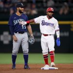 ARLINGTON, TEXAS - AUGUST 18: Yonny Hernandez #65 of the Texas Rangers interacts with Perry Hill #13 of the Seattle Mariners in the bottom of the third inning at Globe Life Field on August 18, 2021 in Arlington, Texas. (Photo by Tom Pennington/Getty Images)