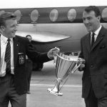 
              FILE  - In this May 16, 1963 file photo, Tottenham Hotspur forwards Jimmy Greaves, right, and Terry Dyson carry the European Cup Winners Cup, at London's Heathrow airport. Spurs defeated Athletico Madrid 5-1 in the European Cup Winners Cup Final becoming the first British club to win the tournament.  Jimmy Greaves, one of England’s greatest goal-scorers who was prolific for Tottenham, Chelsea and AC Milan has died. He was 81. With 266 goals in 379 appearances, Greaves was the all-time record scorer for Tottenham, which announced his death on Sunday, Sept. 19, 2021. (AP Photo/Victor Boynton, File)
            