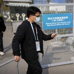 
              Workers wearing face masks to protect against COVID-19 walk past a sign reminding visitors to show proof of a negative coronavirus test within the past 48 hours to enter the Beijing National Aquatics Center, also known as the Water Cube, during the World Wheelchair Curling Championship, a test event for the 2022 Winter Olympics, in Beijing, Friday, Oct. 29, 2021. Beijing Olympic officials say two foreign athletes have tested positive for COVID-19 in ongoing test events for February's Winter Games, Officials also expressed sympathy for a Polish luge competitor who fractured his leg at the Olympics sliding center this week in a crash that has been blamed on human error. (AP Photo/Mark Schiefelbein)
            