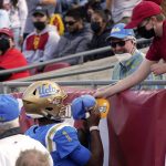 
              UCLA quarterback Dorian Thompson-Robinson, left, signs a hat for a fan after scoring a touchdown during the first half of an NCAA college football game against Southern California Saturday, Nov. 20, 2021, in Los Angeles. (AP Photo/Mark J. Terrill)
            