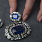 
              A Sotheby's employee holds a historically valuable sapphire and diamond brooch and a pair of ear clips, estimated to sell between 28'000 - 480'000 Swiss francs, during a preview at Sotheby's before auction sale, in Geneva, Switzerland, Tuesday, Nov. 2, 2021. (Salvatore Di Nolfi/Keystone via AP)
            