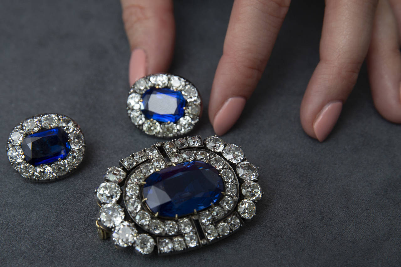 A Sotheby's employee holds a historically valuable sapphire and diamond brooch and a pair of ear cl...