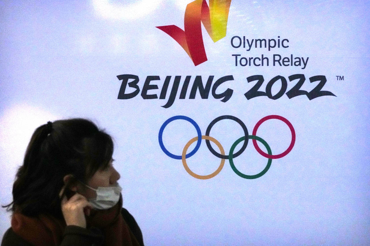 A woman wearing a face mask to protect against COVID-19 walks past the logo for the Beijing 2022 Wi...