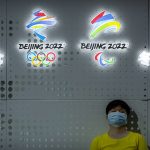 
              FILE - A visitor rests near the logos of the Beijing 2022 Winter Olympics and Paralympics at the China Beijing International High-Tech Expo in Beijing on Sept. 25, 2021. The Beijing Winter Olympics open in just under two months and are now the target to a diplomatic boycott by the United States with others likely to follow. (AP Photo/Mark Schiefelbein, File)
            