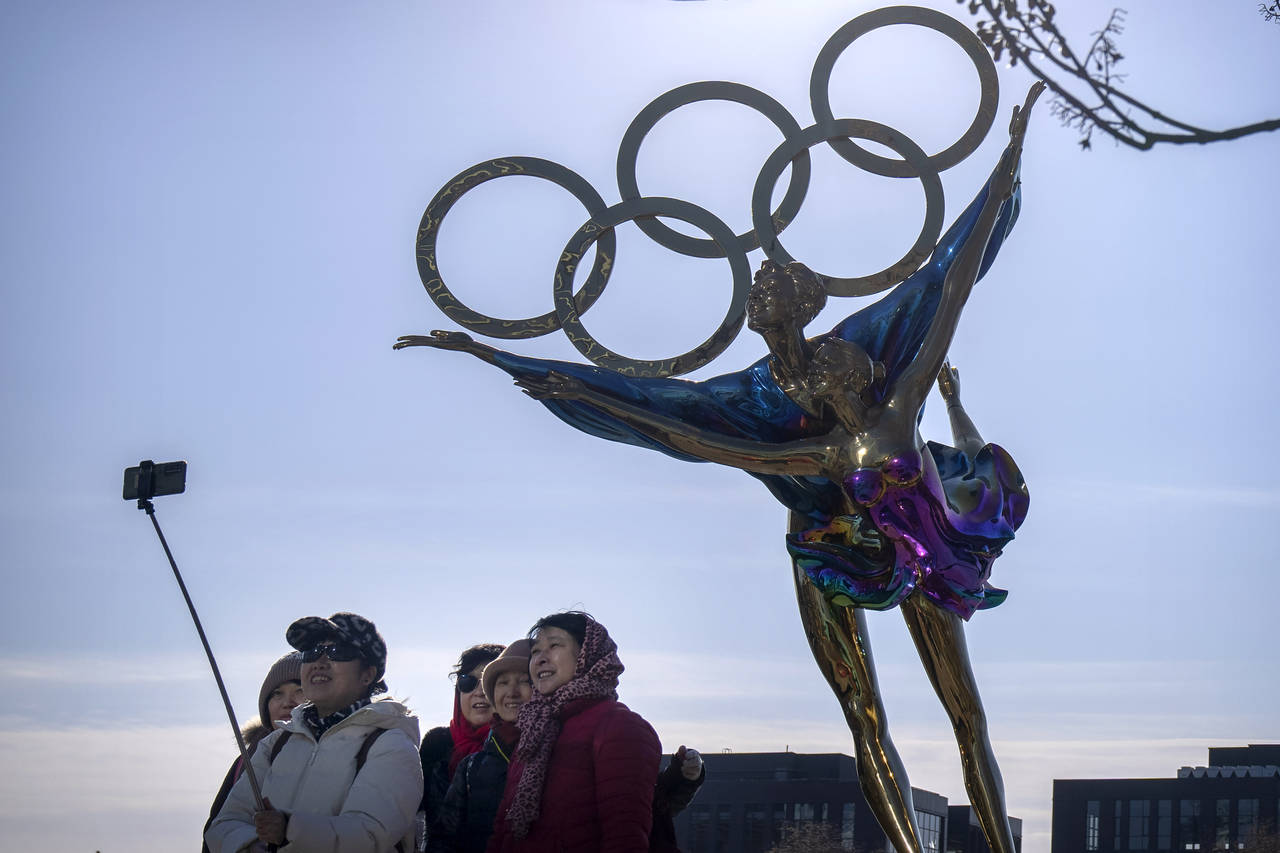 Visitors pose for a selfie with a statue containing the Olympic rings at a park near the headquarte...