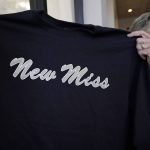 
              Suzi Altman  holds a "New Miss" shirt, Nov. 23, 2021, in Jackson, Miss. The shirt and hats she produces, uses the same the cursive script as the Ole Miss logo that appears on football helmets, sports jerseys, marketing materials and all manner of bags, clothing and other merchandise licensed by the University of Mississippi. Altman applied for the New Miss trademark in July 2020, but the school has filed papers trying to block her from trademarking the "New Miss" logo. (AP Photo/Rogelio V. Solis)
            