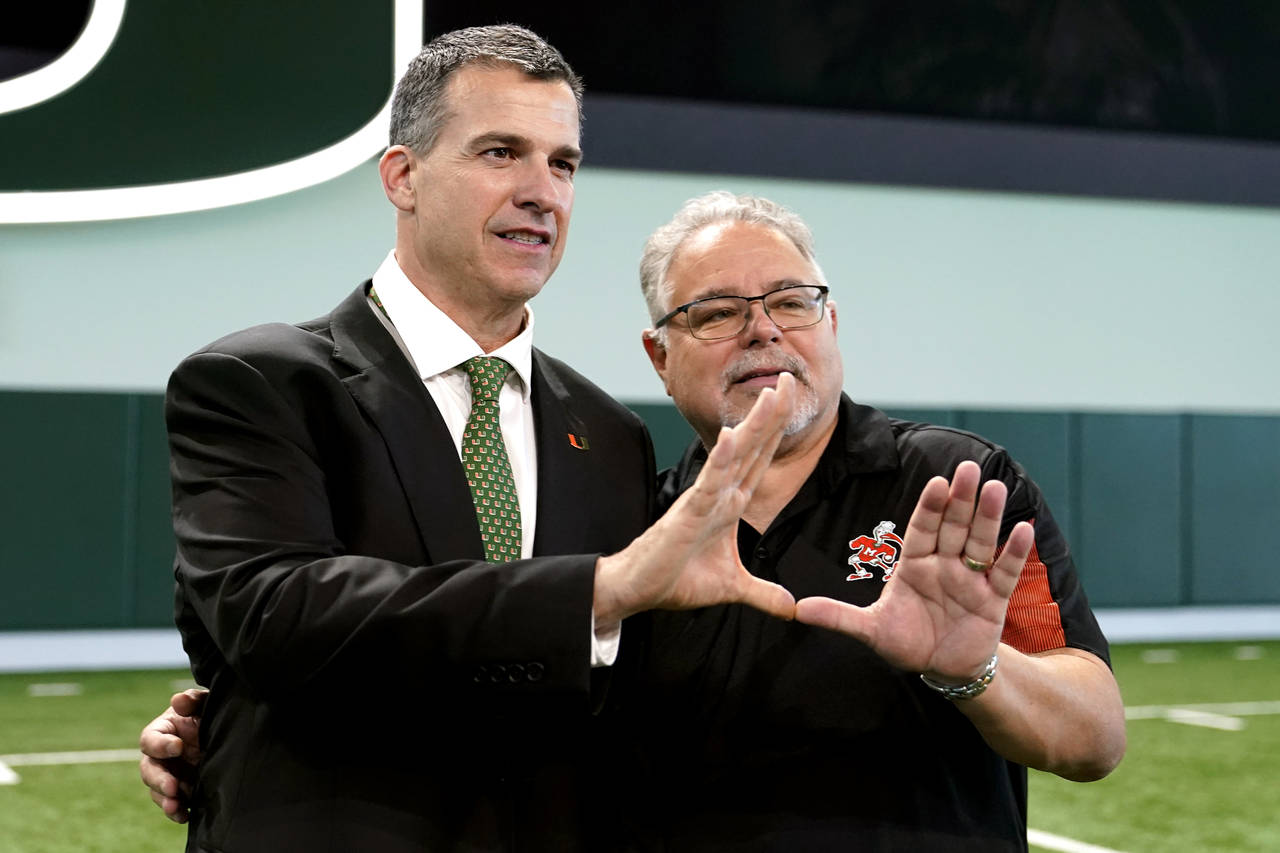 Mario Cristobal, left, Miami's new football coach, makes the sign of the "U" with Harry Rothwell, r...