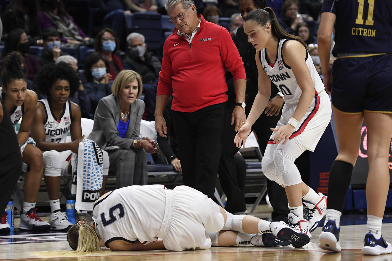 Connecticut's Paige Bueckers stumbles injured as Connecticut's Nika Mühl and head coach Geno Aurie...