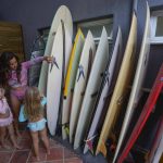 
              Rayana Tanimoto chooses a surf board to practice with her twin daughters Ayala, left, and Eloa, at Maresias beach, in Sao Sebastiao, Brazil, Saturday, Nov. 27, 2021. Earlier that same day, Tanimoto and her twins were catching waves, with each taking turns standing on the same board as their mom. Someday soon, her girls hope to enter competitions. (AP Photo/Andre Penner)
            
