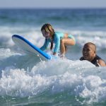 
              Eduardo Tanimoto teaches his five-year-old granddaughter Eloa how to surf at Maresias beach, in Sao Sebastiao, Brazil, Saturday, Nov. 27, 2021. His daughter, Rayana, caught the surfing bug from him. Together, they opened a small hotel on Maresias beach so she could raise her 5-year-old twin daughters, make a living and get in the water as often as possible.  (AP Photo/Andre Penner)
            