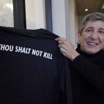 
              Suzi Altman  holds a "New Miss" shirt with the biblical message, "Thou Shalt Not Kill," on its back, Nov. 23, 2021, in Jackson, Miss. The shirt and hats she produces, uses the same the cursive script as the Ole Miss logo that appears on football helmets, sports jerseys, marketing materials and all manner of bags, clothing and other merchandise licensed by the University of Mississippi. Altman applied for the New Miss trademark in July 2020, but the school has filed papers trying to block her from trademarking the "New Miss" logo. (AP Photo/Rogelio V. Solis)
            