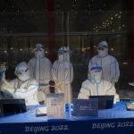 
              FILE - Olympic workers in protective gear work at a credential validation desk at the Beijing Capital International Airport ahead of the 2022 Winter Olympics in Beijing, Jan. 24, 2022. (AP Photo/Jae C. Hong, File)
            