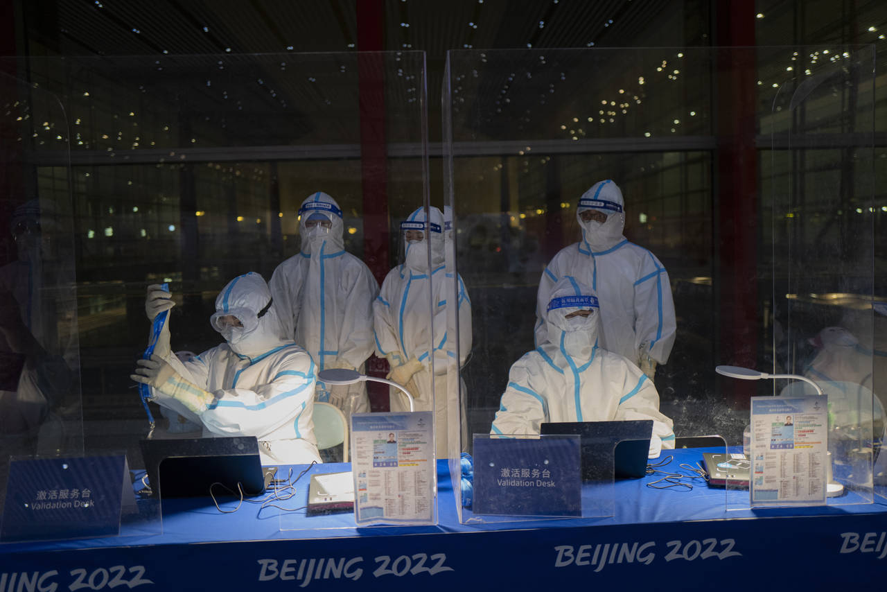 FILE - Olympic workers in hazmat suits work at a credential validation desk at the Beijing Capital ...