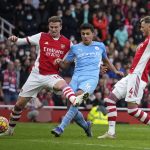 
              Manchester City's Rodrigo, center, shoots to score his sides second goal past Arsenal's Rob Holding, left, and Arsenal's Ben White during the Premier League soccer match between Arsenal and Manchester City at the Emirates Stadium, in London, England, Saturday Jan. 1, 2022. (AP Photo/Matt Dunham)
            