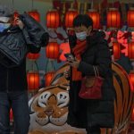 
              A man puts on his face mask to protect from the coronavirus as he and his masked partner take a photo with a tiger decoration, a Chinese zodiac which marks the upcoming year 2022, at a shopping mall in Beijing, Sunday, Jan. 9, 2022. Tianjin, a major Chinese port city near the capital Beijing, began mass testing of its 14 million residents on Sunday, after a cluster of a dozen of children and adults tested positive for COVID-19, including a few with the omicron variant. (AP Photo/Andy Wong)
            
