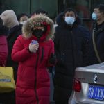
              A woman wearing a face mask to protect from the coronavirus prepares to walk across a street as masked commuters wait for their buses during the morning rush hour in Beijing, Monday, Jan. 10, 2022. Tianjin, a major Chinese city near Beijing has placed its 14 million residents on partial lockdown after a number of children and adults tested positive for COVID-19, including at least two with the omicron variant. (AP Photo/Andy Wong)
            