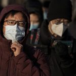 
              A man adjusts his face mask to protect from the coronavirus, walking with masked commuters, as they head to work during the morning rush hour in Beijing, Monday, Jan. 10, 2022. Tianjin, a major Chinese city near Beijing has placed its 14 million residents on partial lockdown after a number of children and adults tested positive for COVID-19, including at least two with the omicron variant. (AP Photo/Andy Wong)
            