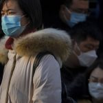 
              A woman wearing a face mask to protect from the coronavirus walks by masked commuters getting out of a bus during the morning rush hour in Beijing, Monday, Jan. 10, 2022. Tianjin, a major Chinese city near Beijing has placed its 14 million residents on partial lockdown after a number of children and adults tested positive for COVID-19, including at least two with the omicron variant. (AP Photo/Andy Wong)
            