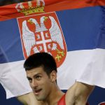 
              FILE - Novak Djokovic, of Serbia, hoists his country's flag after beating James Blake, of the United States, during their bronze medal match for men's singles tennis at the Beijing 2008 Olympics in Beijing, Aug. 16, 2008. In Serbia, Djokovic is revered as a national hero who overcame the odds in the economically crippled country with few tennis courts to become the world’s No. 1 player. (AP Photo/Charles Krupa, File)
            