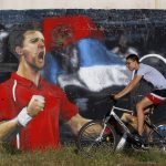 
              FILE - A boy riding a bike passes a graffiti of Serbian tennis player Novak Djokovic in Belgrade, Serbia, Aug. 8, 2013. In Serbia, Djokovic is revered as a national hero who overcame the odds in the economically crippled country with few tennis courts to become the world’s No. 1 player. (AP Photo/Darko Vojinovic, File)
            
