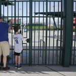 
              FILE - Cubs fans take photos through the locked gates at Sloan Park, the spring training site of the Chicago Cubs, in Mesa, Ariz., after Major League Baseball suspended the rest of its spring training game schedule because of the coronavirus outbreak, Friday, March 13, 2020. Spring training games might not count in the official standings, but they certainly count for the pocketbooks of business owners in Arizona and Florida. They're also a much-anticipated destination for fans who come for the warm sunshine and the laid-back atmosphere. (AP Photo/Sue Ogrocki, File)
            