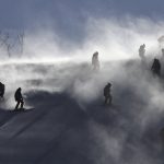 
              FILE - Course crew are shrouded in snow as they carry ski gates after the women's giant slalom was postponed due to high winds at the 2018 Winter Olympics at the Yongpyong Alpine Center, Pyeongchang, South Korea, Feb. 12, 2018. Winter Olympians in outdoor sports such as Alpine skiing or snowboarding say the weather can be a key factor in success or failure. (AP Photo/Christophe Ena, File)
            