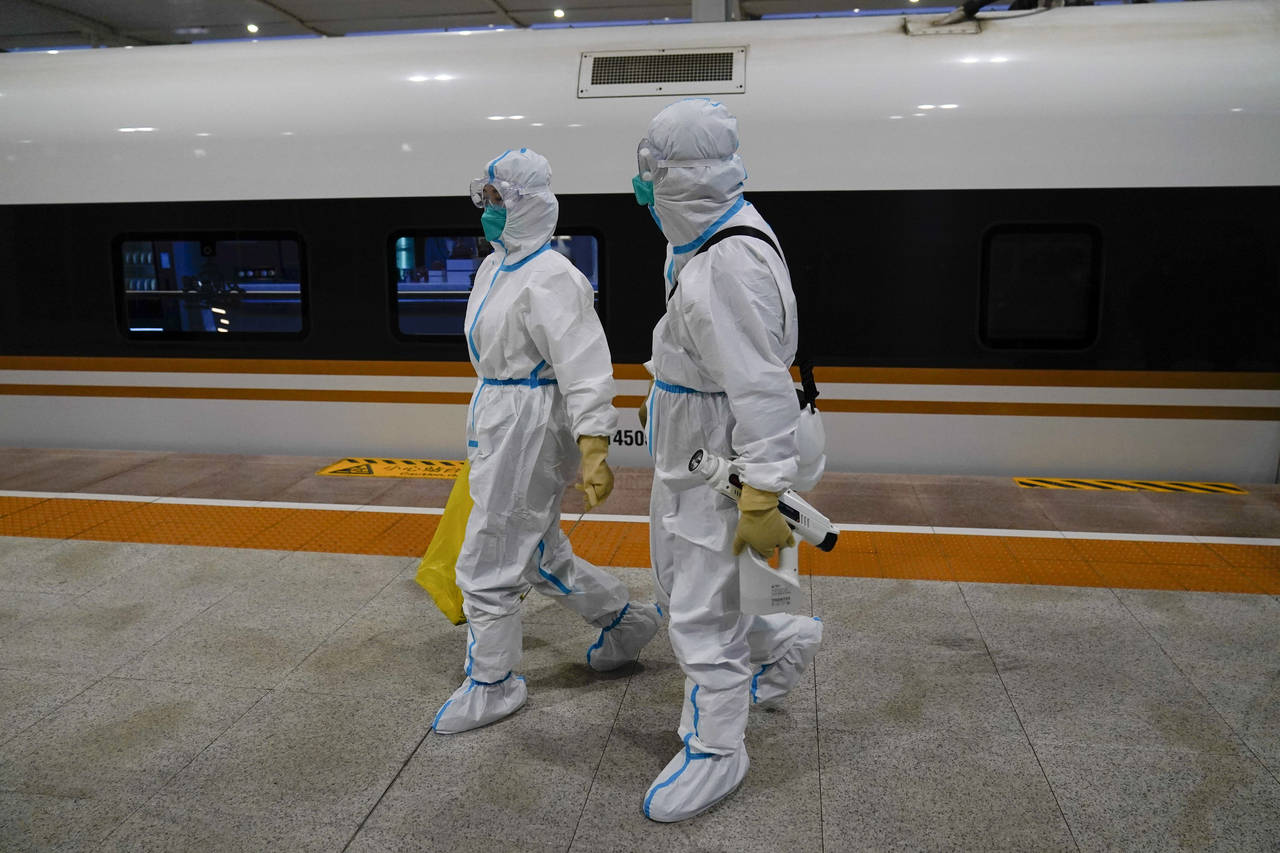 Two workers in protective gear walk way from a train car designated for Olympic workers after disin...