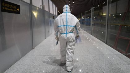 FILE - A member of airport personnel dressed in protective gear leads passengers into the customs a...