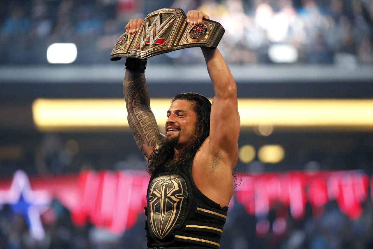 FILE - Roman Reigns holds up the championship belt after defeating Triple H during WrestleMania 32 ...