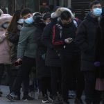 
              A man wearing a face mask to protect from the coronavirus walks through a line of masked commuters waiting for their buses as they head to work during the morning rush hour in Beijing, Monday, Jan. 10, 2022. Tianjin, a major Chinese city near Beijing has placed its 14 million residents on partial lockdown after a number of children and adults tested positive for COVID-19, including at least two with the omicron variant. (AP Photo/Andy Wong)
            