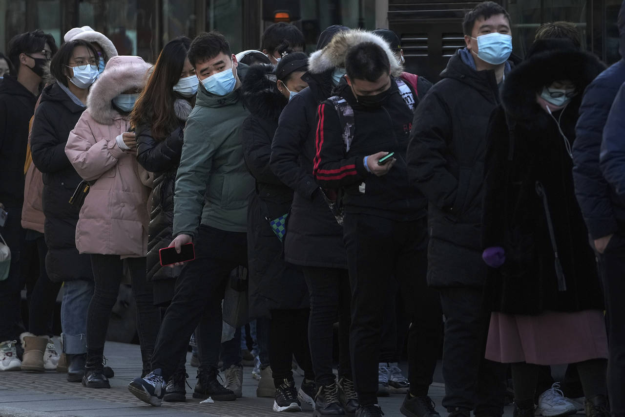 A man wearing a face mask to protect from the coronavirus walks through a line of masked commuters ...