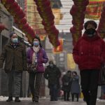 
              Visitors wearing face masks to help protect from the coronavirus walk by lanterns on display at Qianmen Street, a popular tourist spot in Beijing, Sunday, Jan. 23, 2022. Chinese authorities have called on the public to stay where they are during the Lunar New Year instead of traveling to their hometowns for the year's most important family holiday. (AP Photo/Andy Wong)
            