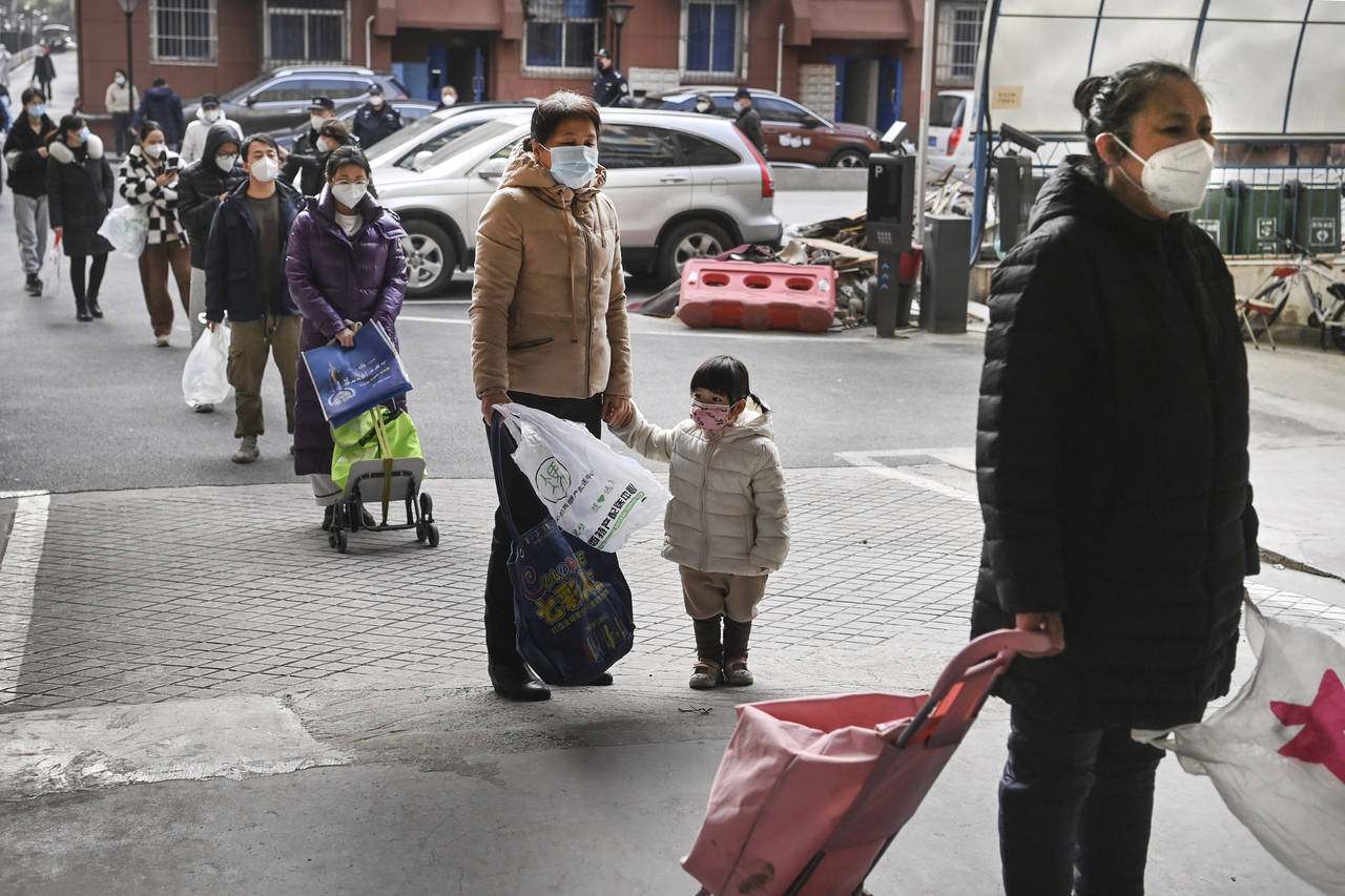 In this photo released by Xinhua News Agency, residents wearing masks line up to receive necessitie...