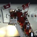 
              Alabama players get off a plane, walking past flag-wavers at an airport in Indianapolis on Friday, Jan. 7, 2022. Alabama is scheduled to play Georgia on Monday in the College Football Playoff championship game. (Curtis Compton/Atlanta Journal-Constitution via AP)
            