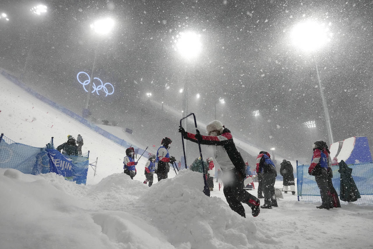 Volunteers clear the course as the women's aerials qualification has been delayed due to a weather ...