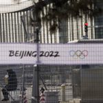 
              FILE - Two security personnel are seen through fences outside the main media center at the 2022 Winter Olympics, Jan. 26, 2022, in Beijing. (AP Photo/Jae C. Hong, File)
            