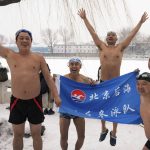 
              Swimmers from the Beijing Houhai Happy Winter Swimming Team cheer with their banner before swimming in the half-frozen waters of the Shichahai Lake during a snow fall in Beijing, Sunday, Feb. 13, 2022. The swimmers range in age from 20 to 90. Some come every day, rain or shine, smog or clear skies. (AP Photo/Andy Wong)
            