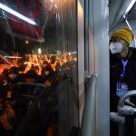 
              A journalist looks out the window of an Olympic shuttle bus as performers walk along the street with props used at the opening ceremony of the 2022 Winter Olympics, Saturday, Feb. 5, 2022, in Beijing. (AP Photo/Jae C. Hong)
            