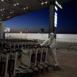 
              An Olympic worker wearing a protective suit pushes trolleys at the Beijing Capital International Airport after the 2022 Winter Olympics, Monday, Feb. 21, 2022, in Beijing. (AP Photo/Natacha Pisarenko)
            