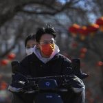
              Residents wearing face masks to help protect from the coronavirus ride an electric scooter along a street decorated with red lanterns in Beijing, Tuesday, Feb. 8, 2022. China has ordered inhabitants of the southern city of Baise to stay home and suspended transportation links amid a surge in COVID-19 cases at least partly linked to the omicron variant. (AP Photo/Andy Wong)
            
