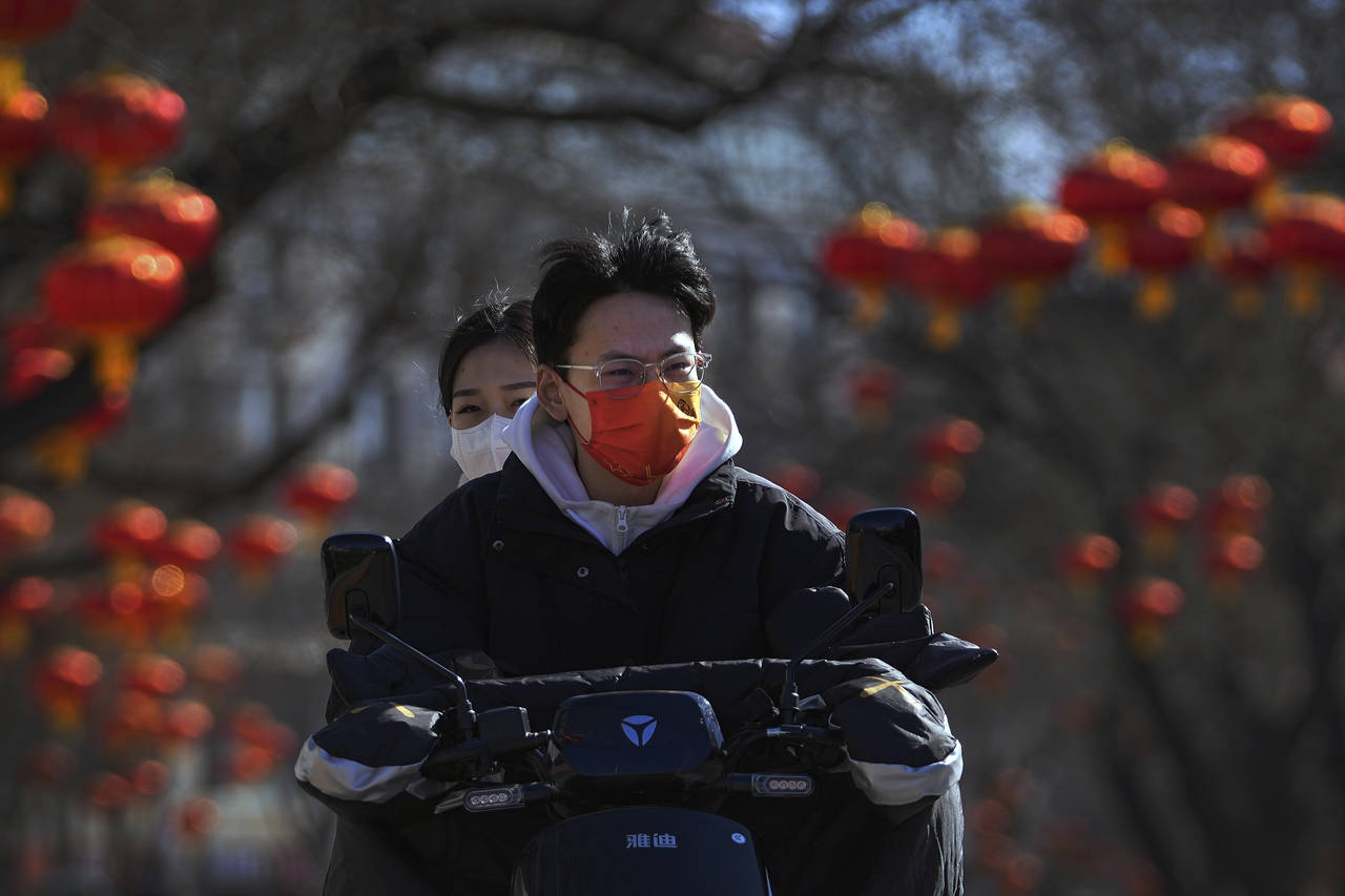 Residents wearing face masks to help protect from the coronavirus ride an electric scooter along a ...