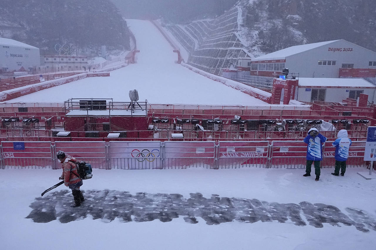 A worker clears snow from the stands in the finish area at the alpine ski venue at the 2022 Winter ...