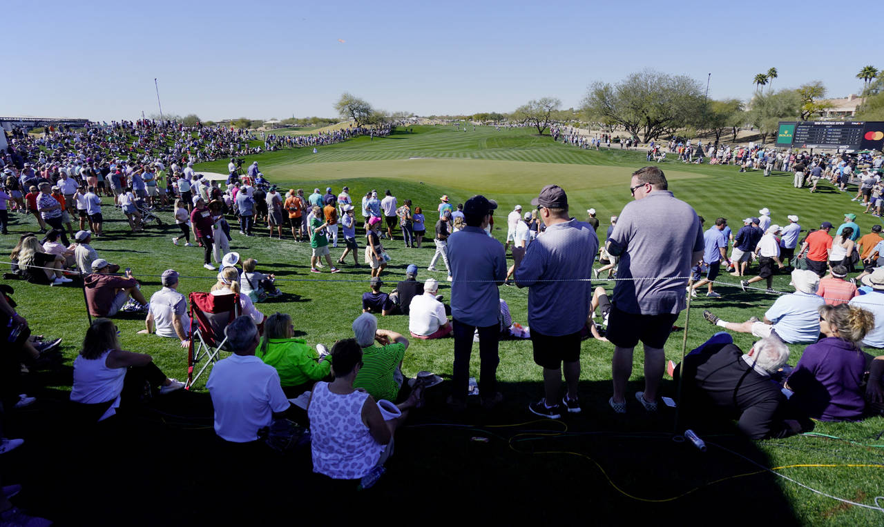 Fans circle the ninth hole as groups make their way up the fairway during the Phoenix Open golf tou...