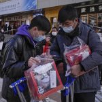 
              People inspect their purchases outside a store selling 2022 Winter Olympics memorabilia in Beijing, Monday, Feb. 7, 2022. The race is on to snap up scarce 2022 Winter Olympics souvenirs. Dolls of mascot Bing Dwen Dwen, a panda in a winter coat, sold out after buyers waited in line overnight in freezing weather. (AP Photo/Andy Wong)
            